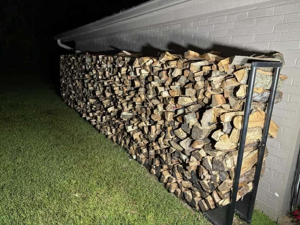 Split firewood stacked high in a long rack along a house wall