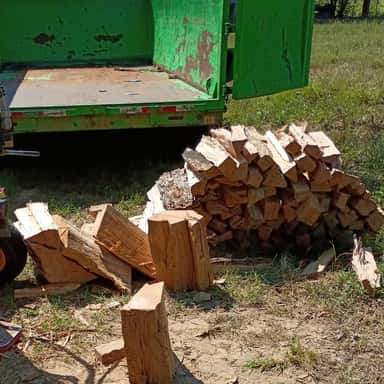 Freshly split firewood piled beside a green dump trailer at the wood yard